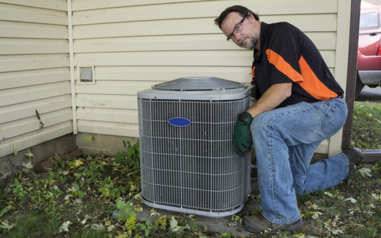 Repairman cleaning outside air conditioner unit grill.